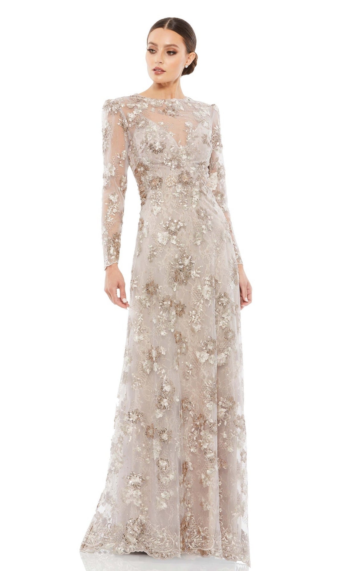 A woman stands wearing the Long Mocha Lace Formal Dress by Mac Duggal 67875—an elegant gown with sheer fabric, metallic floral embroidery, long sleeves, and a high neckline, perfect for the mother of the bride.